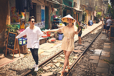 Buy stock photo Shot of a young couple walking on the train tracks through the streets of Vietnam