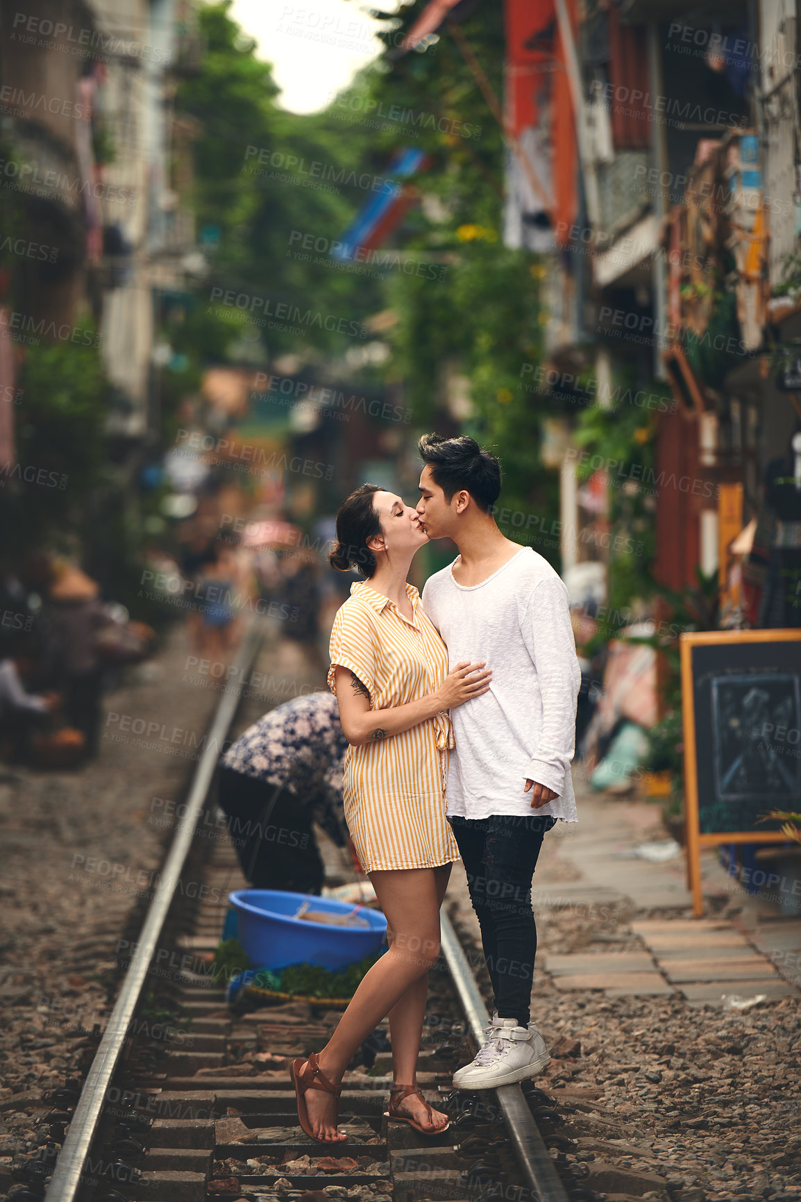 Buy stock photo Travel, kiss and couple on train tracks in Vietnam for holiday, vacation and tourist destination. Holding hands, love and man and woman on railway for adventure, journey and bonding in urban city