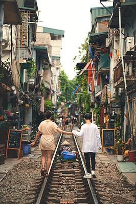 Buy stock photo Rearview shot of a young couple walking on the train tracks through the streets of Vietnam