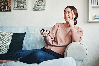 Buy stock photo Cropped shot of an attractive young woman sitting on her home sofa alone and using a television remote control