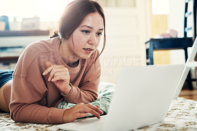 Buy stock photo Cropped shot of an attractive young woman lying on her living room floor and using her laptop