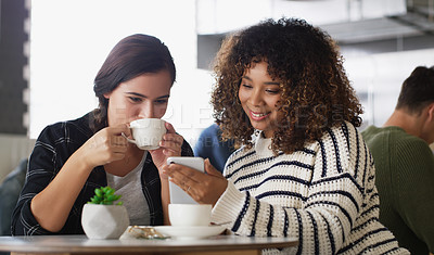 Buy stock photo Shot of two young women looking at something on a cellphone in a cafe