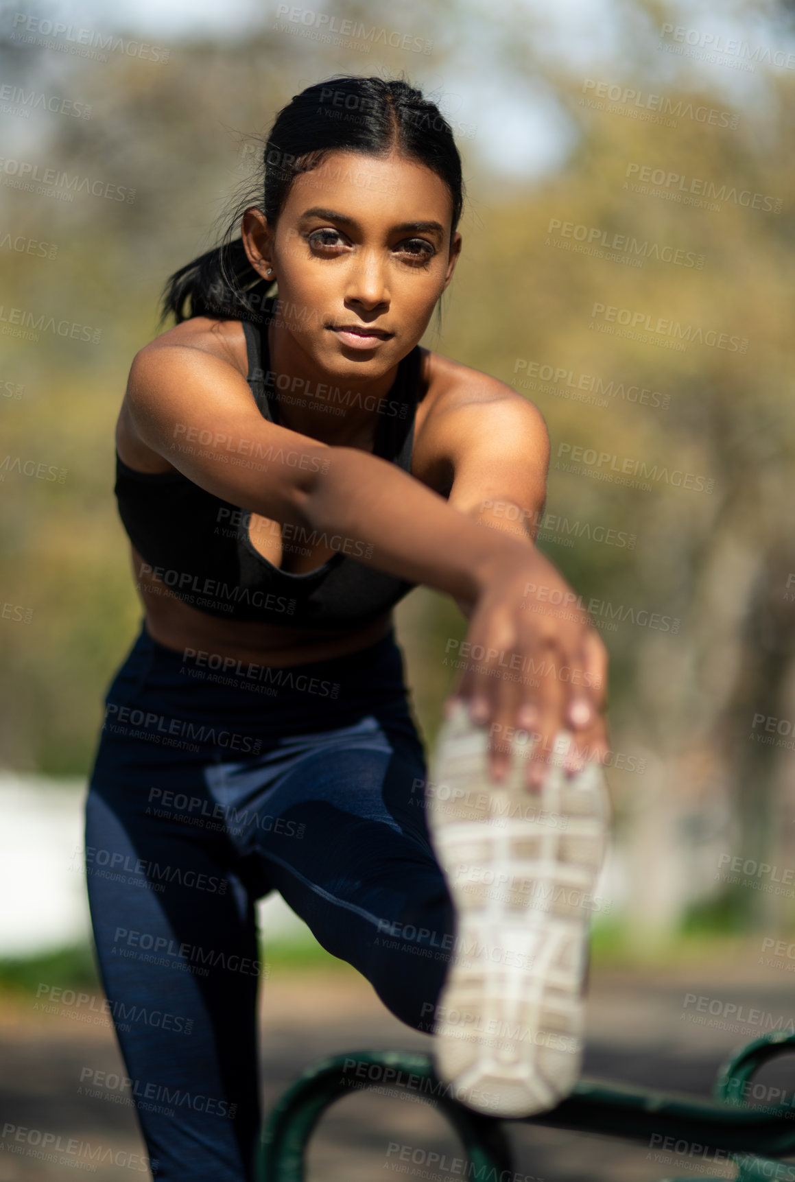 Buy stock photo Portrait of a sporty young woman stretching her legs while exercising outdoors