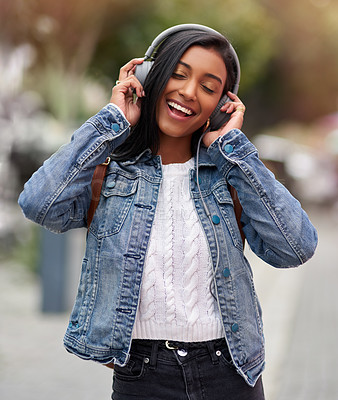 Buy stock photo Cropped shot of a young woman listening to music through her headphones while walking outdoors