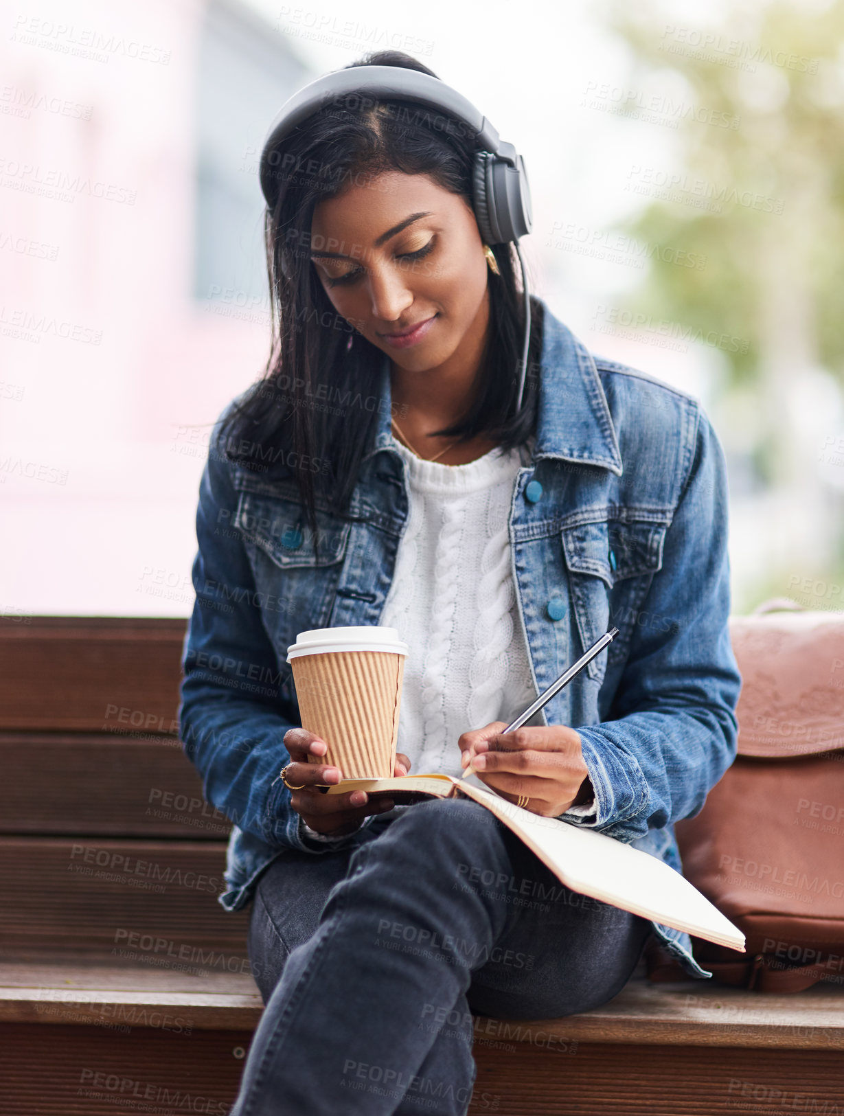 Buy stock photo Outdoor, student or Indian woman writing in diary for knowledge, notes or learning on bench. Headphones, coffee and writer in city studying college info on journal notebook for schedule checklist