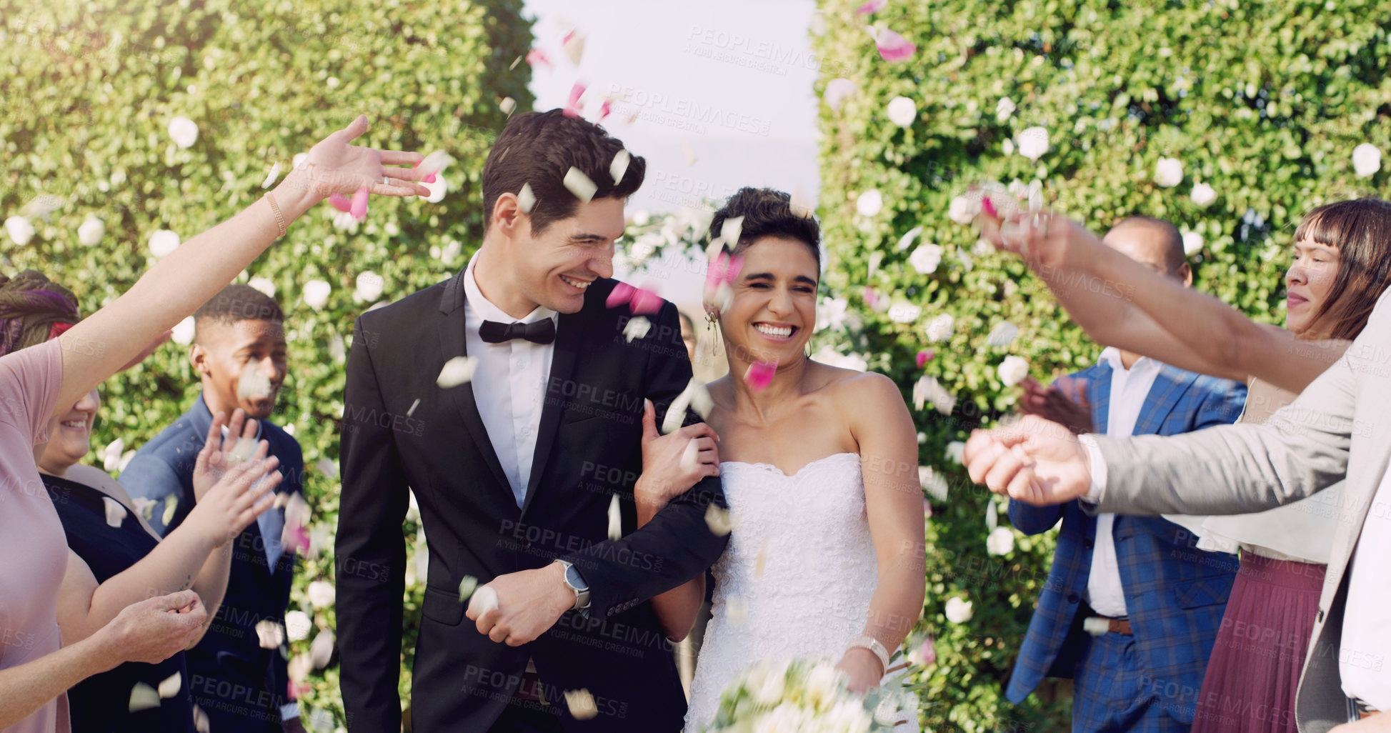 Buy stock photo Cropped shot of an affectionate young newlywed couple leaving their wedding venue with their guests throwing confetti in the background