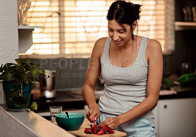 Buy stock photo Shot of a young woman making a healthy snack with strawberries at home