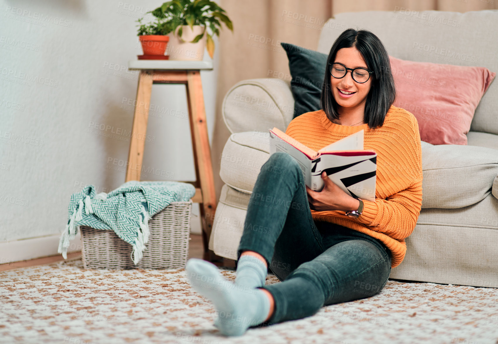 Buy stock photo Shot of a young woman relaxing on the floor in the living room and reading a book at home