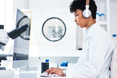 Buy stock photo Shot of a young scientist wearing headphones while working on a computer in a lab