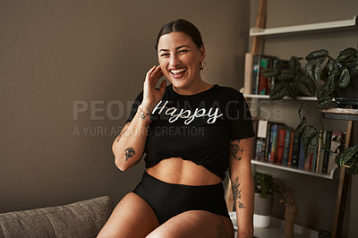 Buy stock photo Cropped portrait of an attractive young woman smiling while sitting on her couch at home