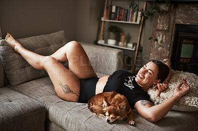 Buy stock photo Full length shot of an attractive young woman smiling while lying next to her dog on her couch at home