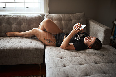 Buy stock photo Full length portrait of an attractive young woman smiling while using a smartphone on her couch at home