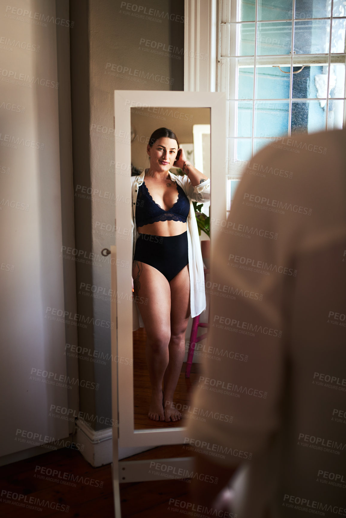 Buy stock photo Cropped shot of an attractive young woman admiring herself in the mirror in her bedroom at home