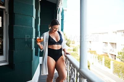 Buy stock photo Cropped shot of an attractive young woman smiling while holding a glass of tea on her balcony in the morning