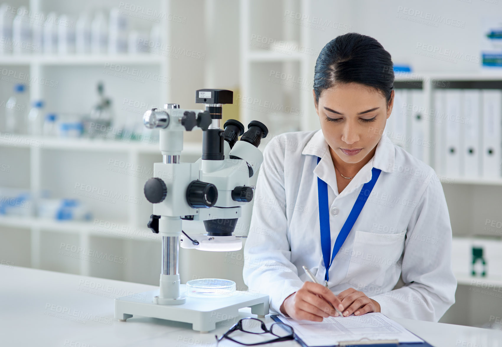 Buy stock photo Shot of a young woman filling out paperwork while working a laboratory