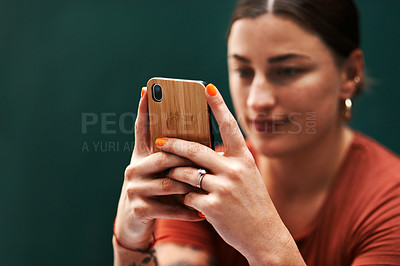 Buy stock photo Cropped shot of an attractive young businesswoman sitting alone against a green background and texting on her cellphone