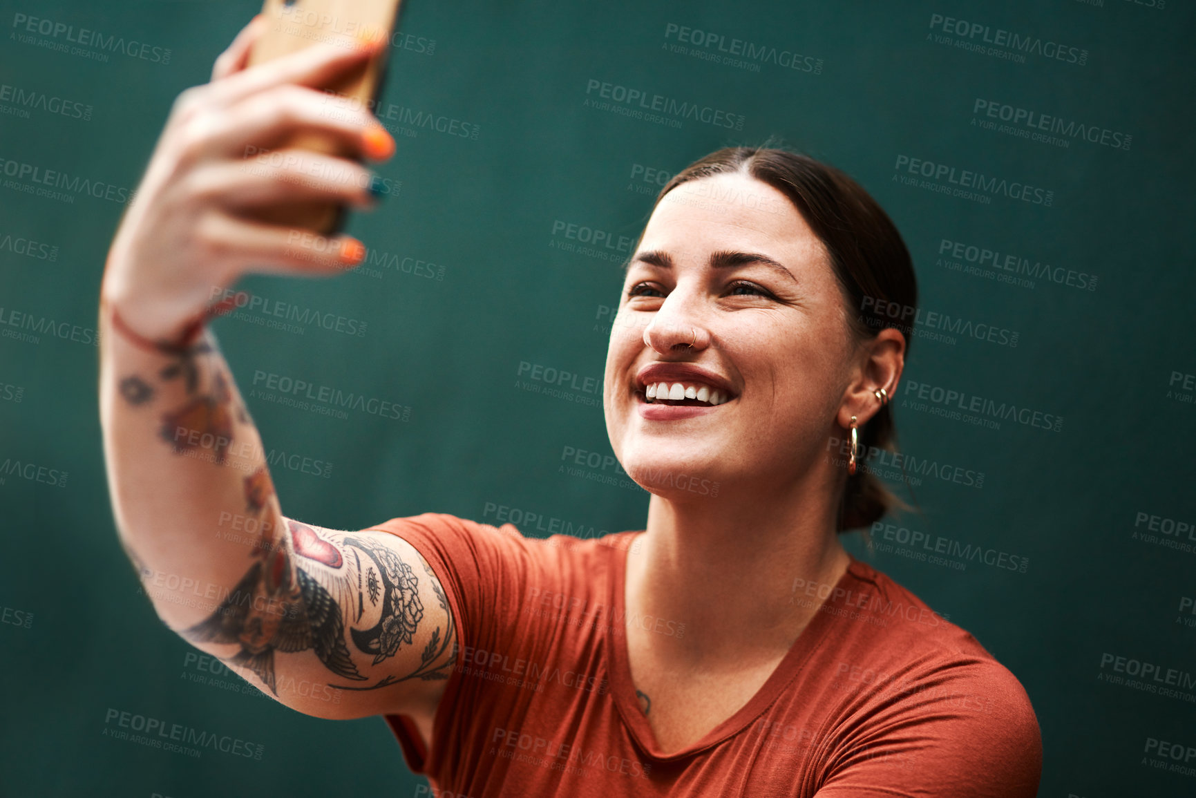 Buy stock photo Cropped shot of an attractive young businesswoman sitting alone against a green background and using her cellphone to take selfies