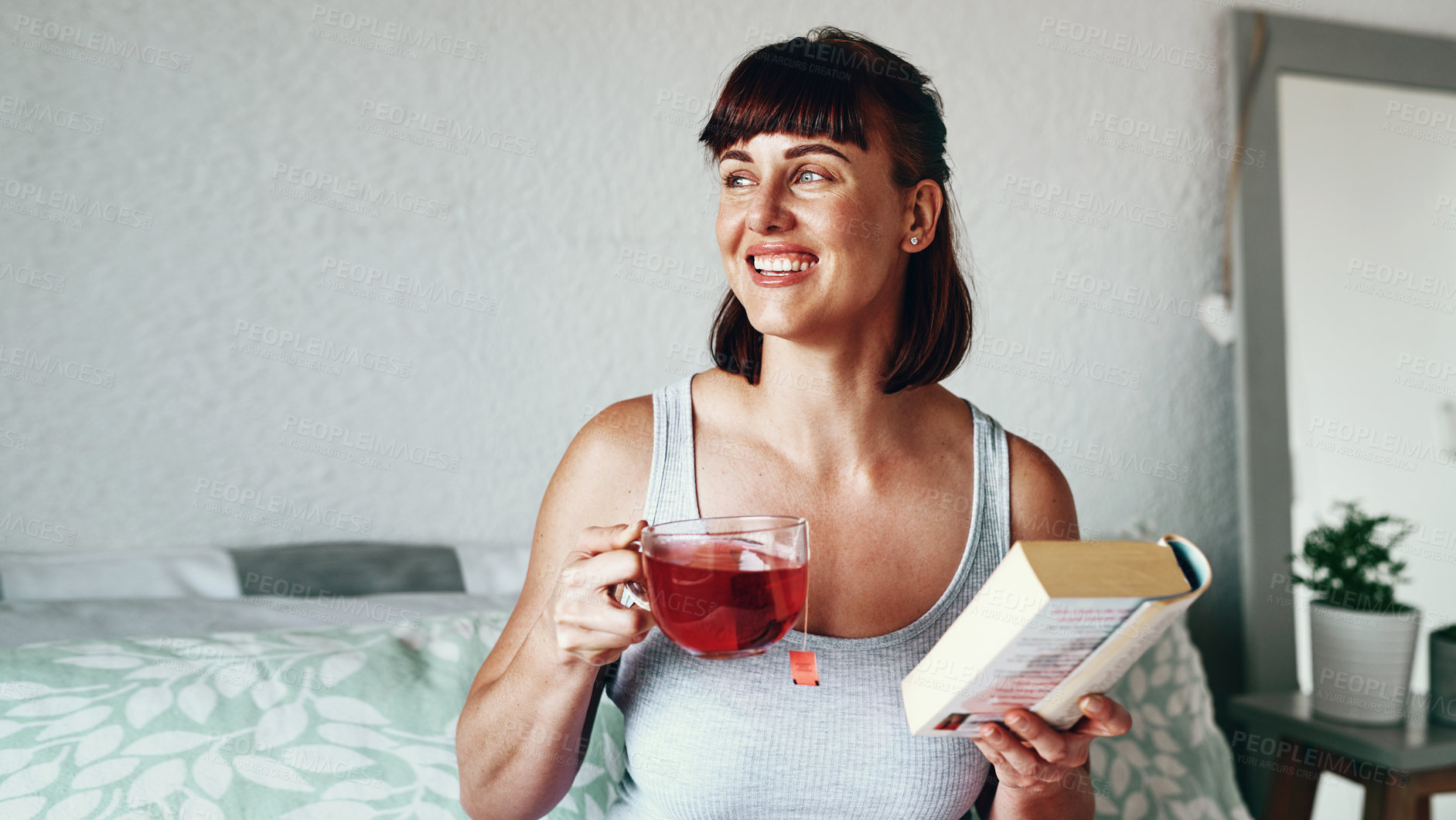 Buy stock photo Shot of an attractive young woman drinking tea and reading a book in her bedroom at home
