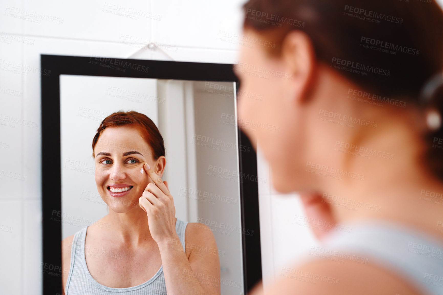 Buy stock photo Shot of an at attractive young woman applying moisturizer on her face in her bathroom at home