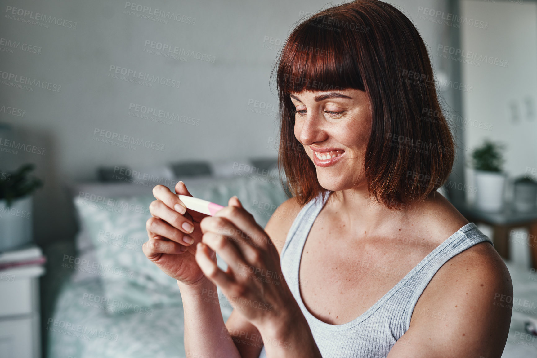 Buy stock photo Shot of an attractive young woman feeling happy while looking at her pregnancy test results at home