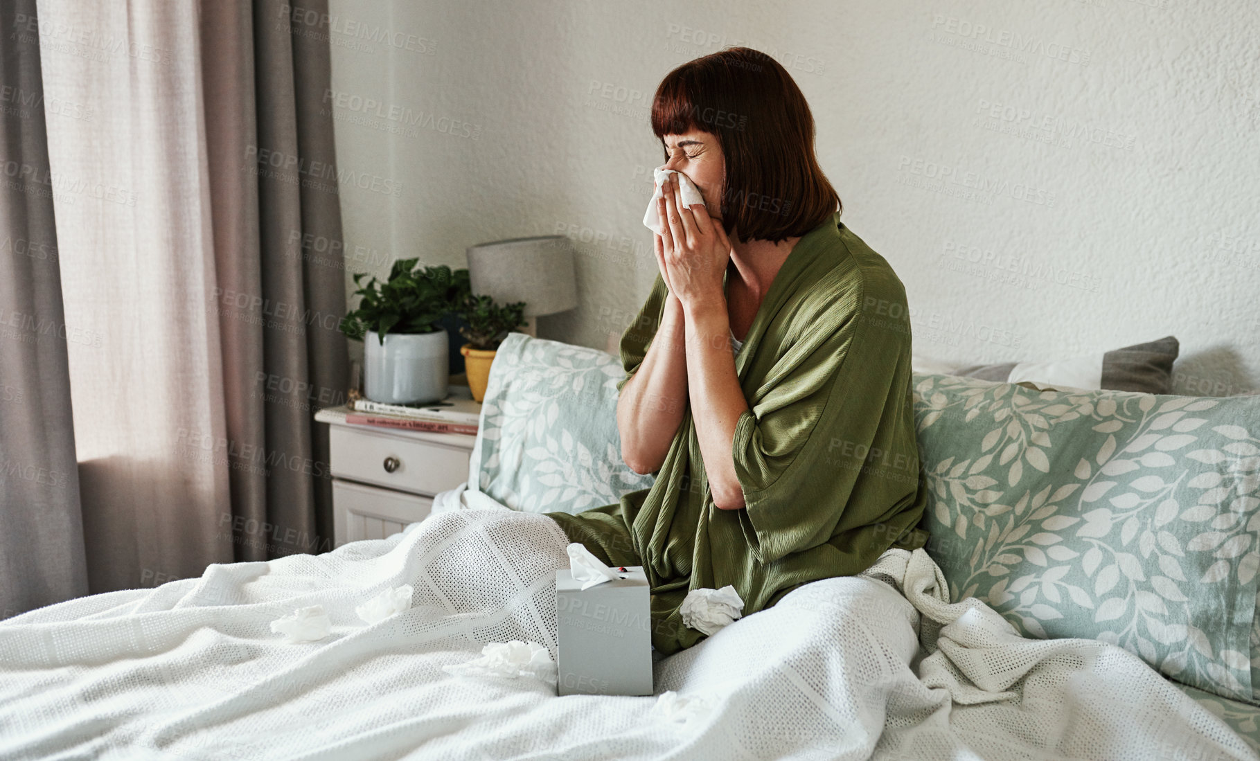 Buy stock photo Shot of an attractive young woman feeling sick and blowing her nose with a tissue inside her bedroom at home