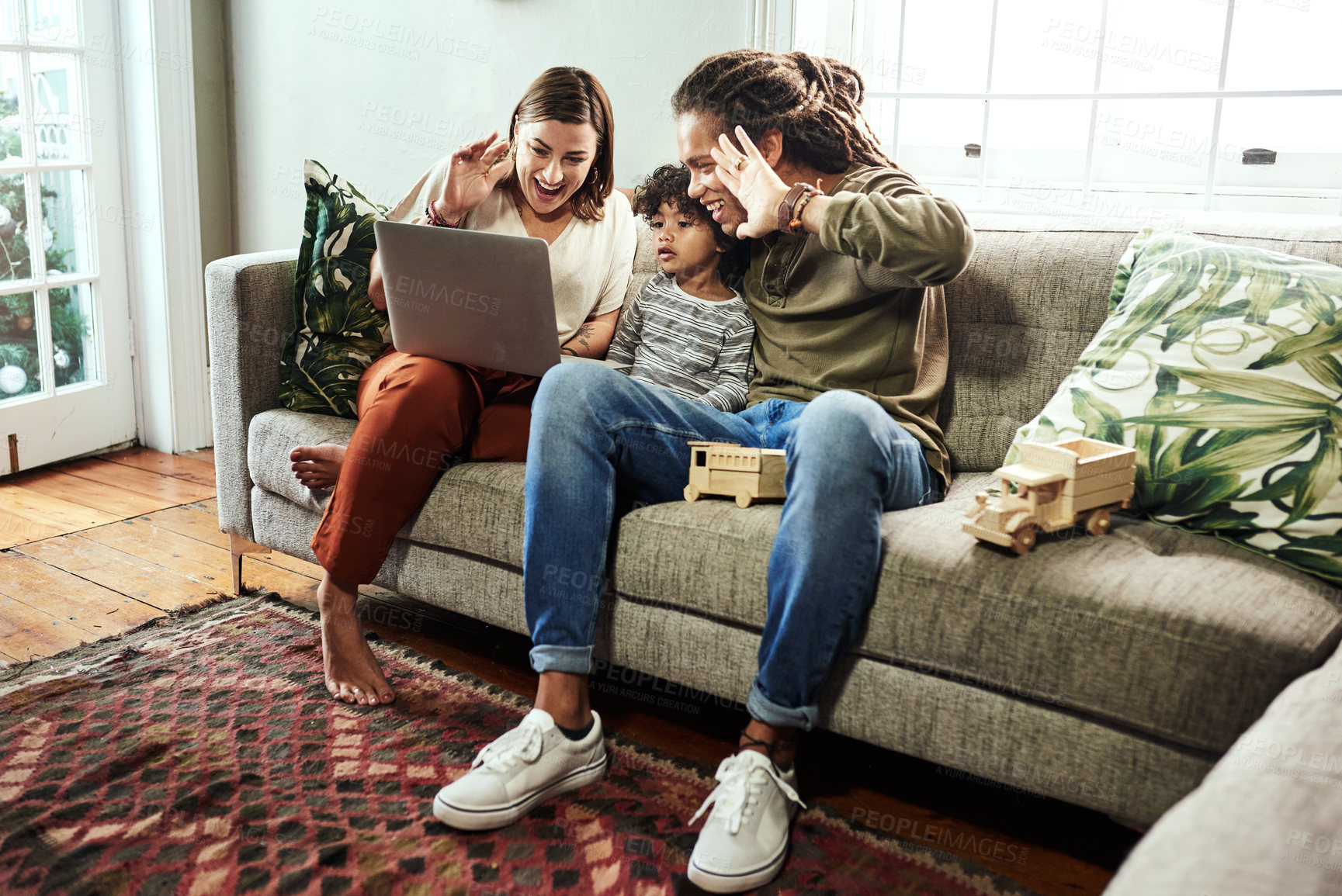 Buy stock photo Shot of a cheerful young couple and their son having a video call to relatives on a laptop while being seated on a sofa at home
