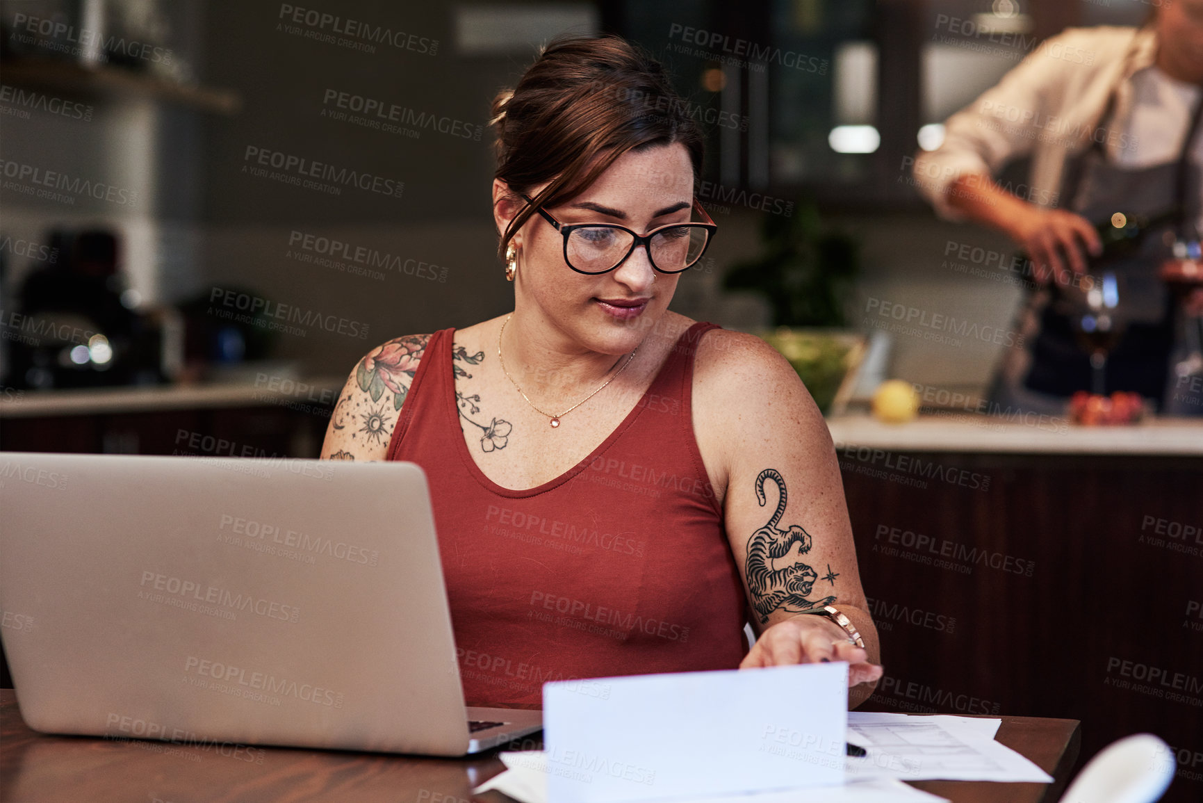 Buy stock photo Cropped shot of a cheerful young woman working on a laptop and doing paperwork while being seated at a table at home