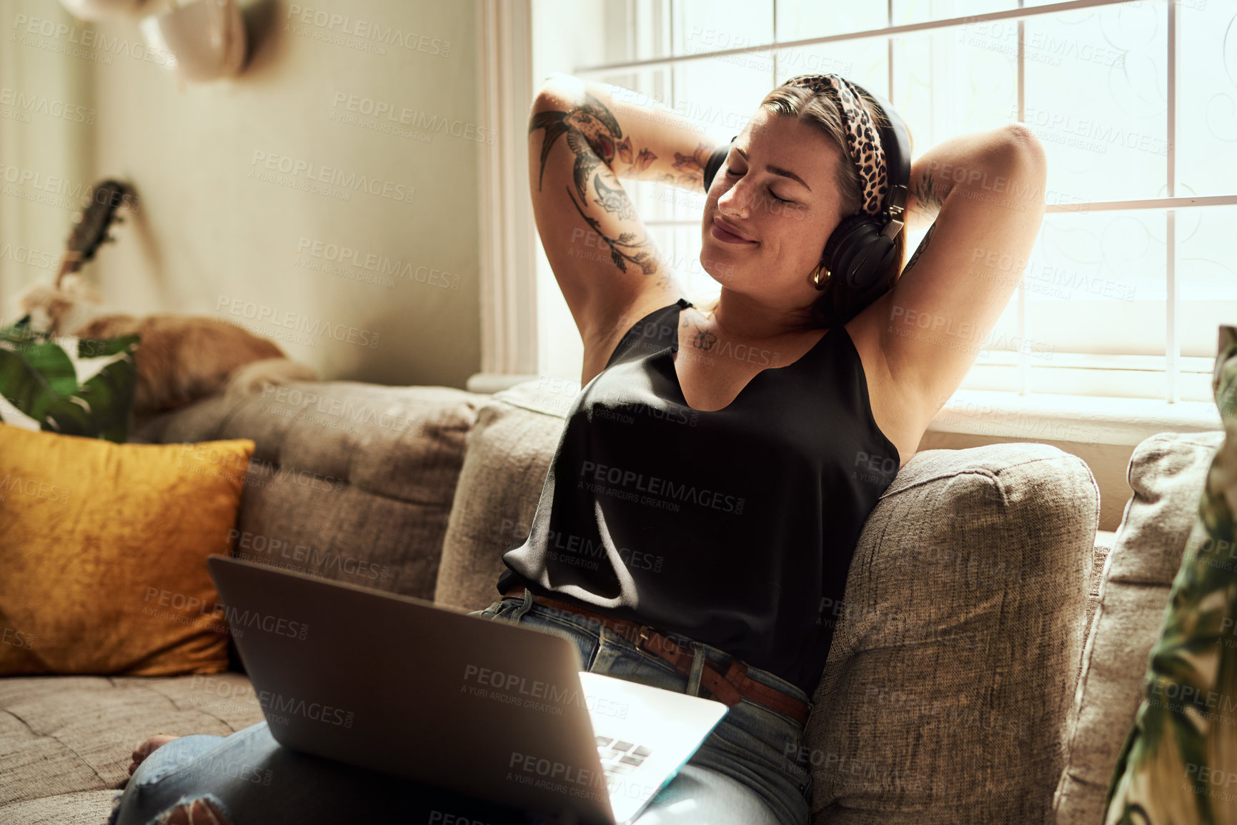 Buy stock photo Shot of a young woman using a laptop and headphones on the sofa at home
