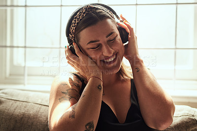 Buy stock photo Shot of a young woman using headphones on the sofa at home