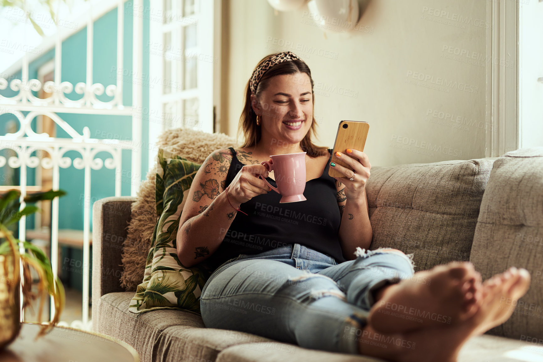 Buy stock photo Shot of a young woman having coffee and using a smartphone on the sofa at home