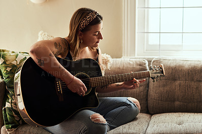 Buy stock photo Shot of a young woman playing a guitar on a relaxing day at home