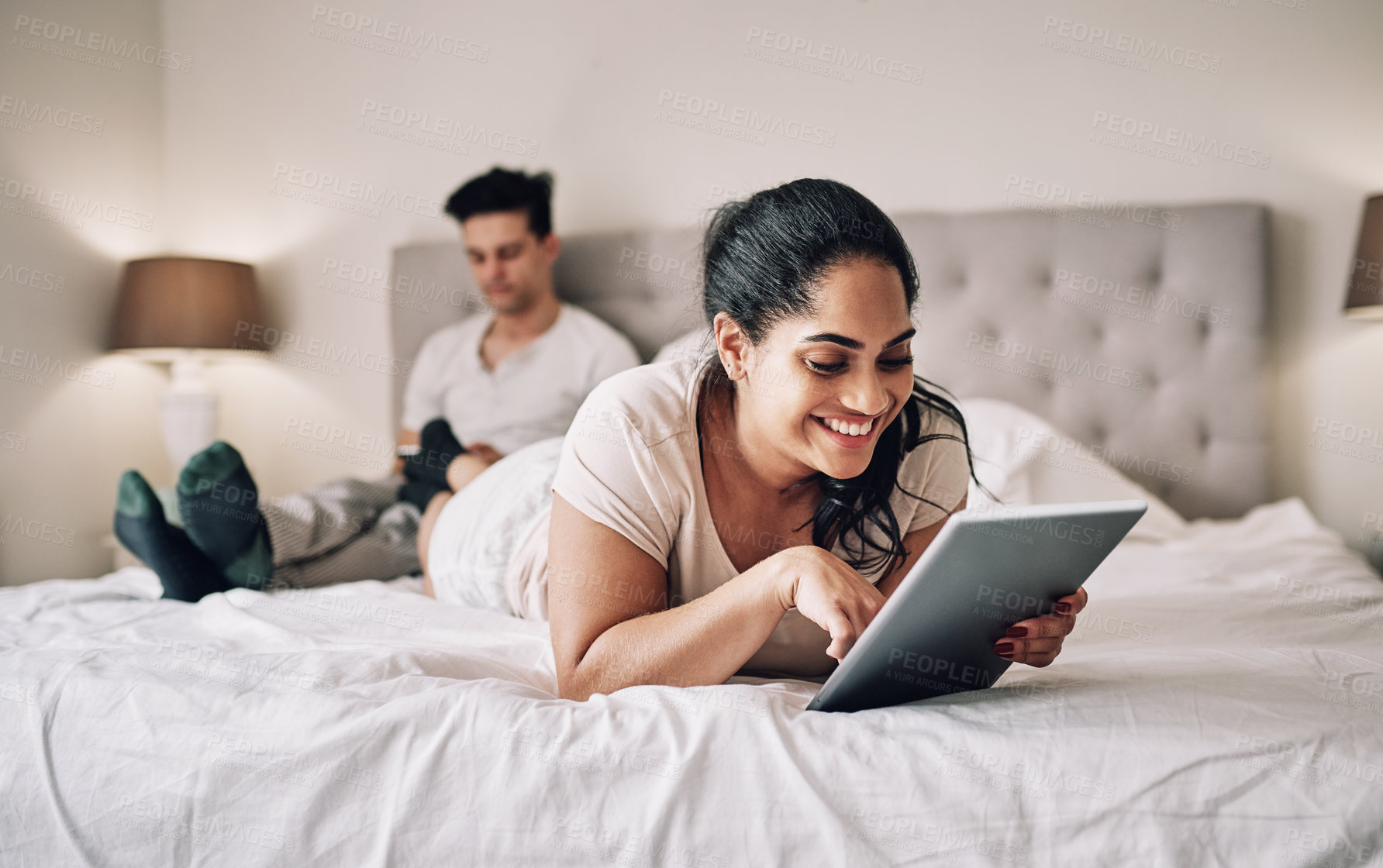 Buy stock photo Shot of a young woman using a digital tablet while her boyfriend sits in the background