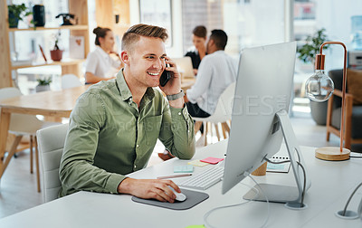 Buy stock photo Cropped shot of a handsome young businessman sitting and using his cellphone while using his computer in the office