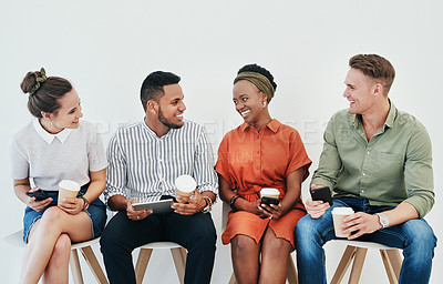 Buy stock photo Cropped shot of a diverse group of businesspeople sitting against a gray background together and using technology in the office