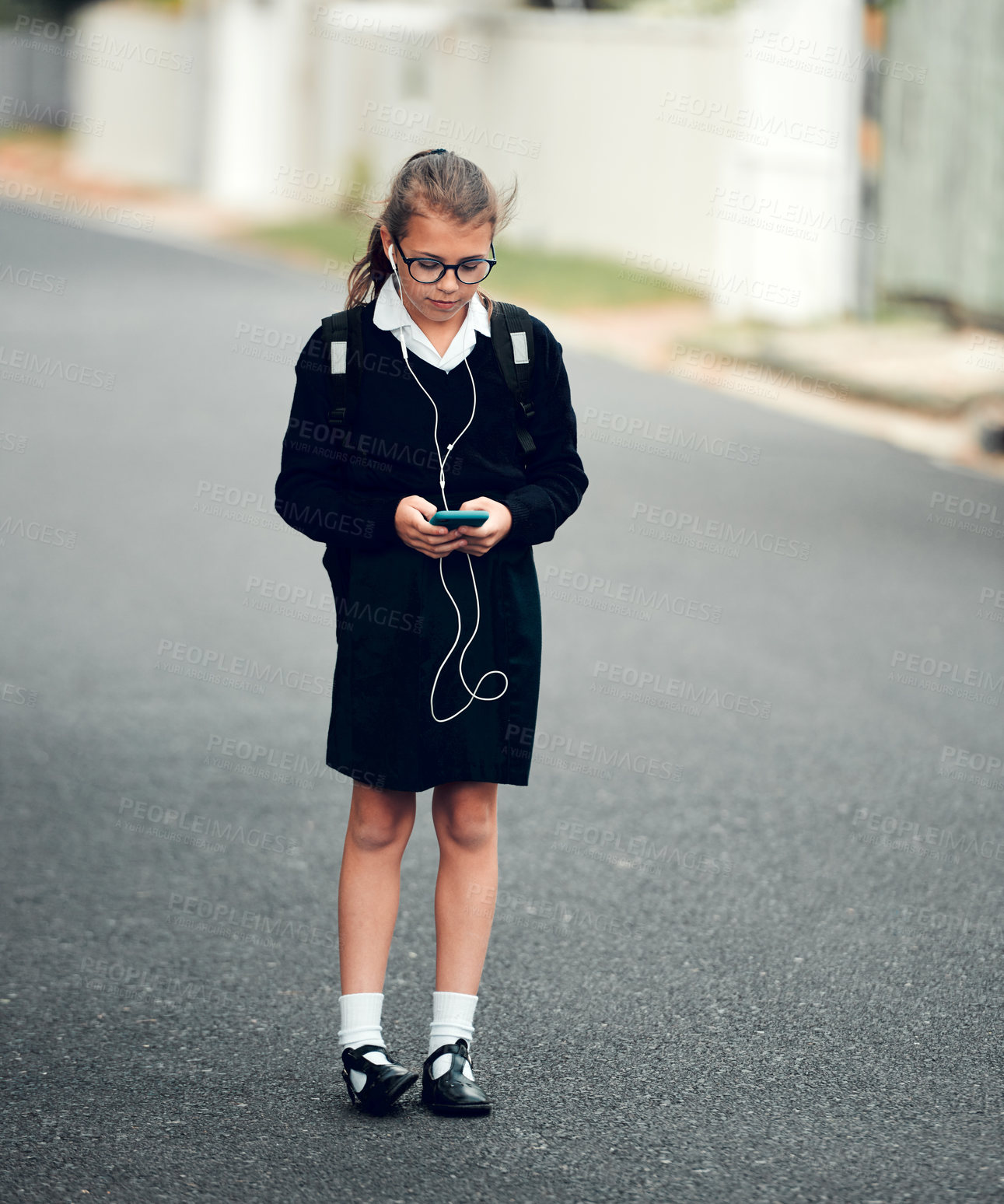 Buy stock photo Full length shot of a young schoolgirl listening to music and using her cellphone while walking to school