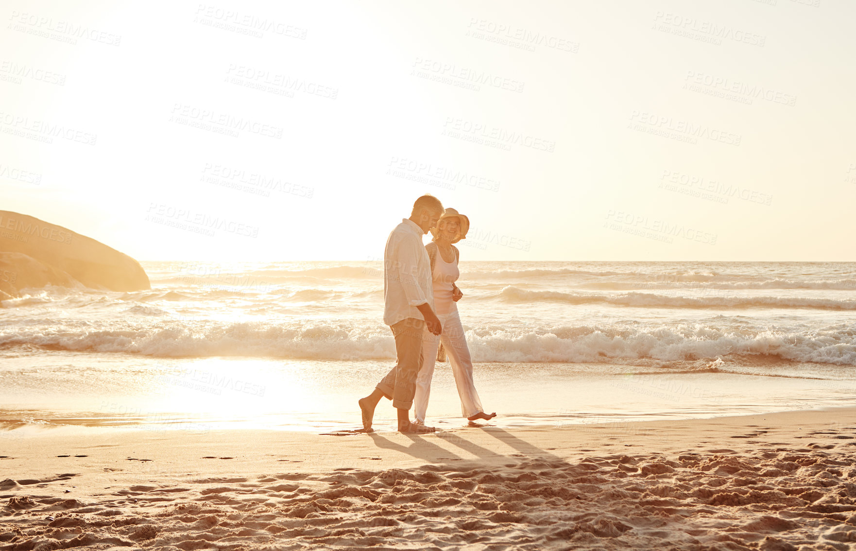 Buy stock photo Full length shot of an affectionate middle aged couple walking hand in hand along the beach at sunset