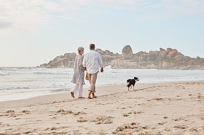 Buy stock photo Rearview shot of an affectionate middle aged couple walking hand in hand with along the beach with their dog