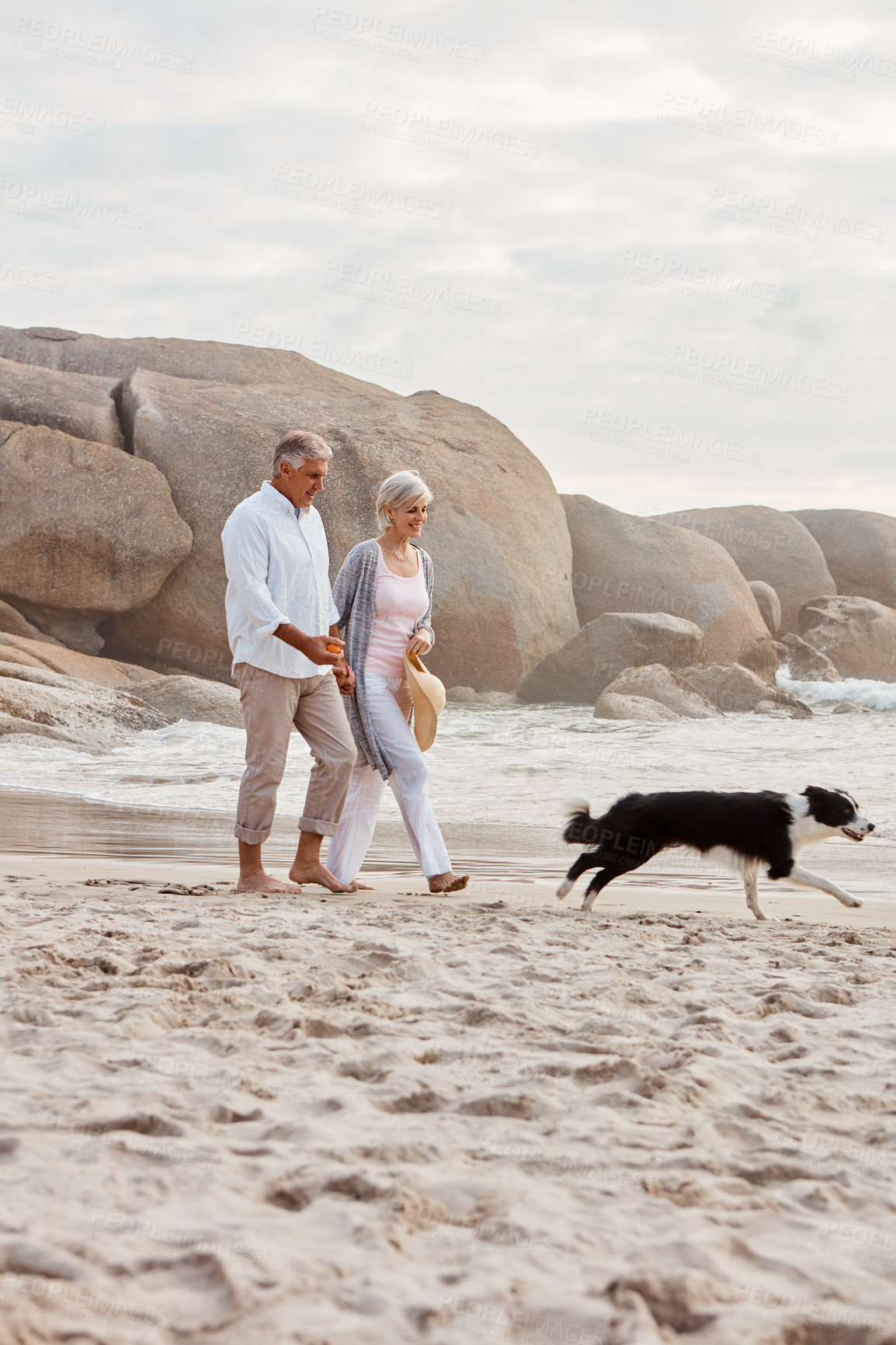 Buy stock photo Full length shot of an affectionate middle aged couple walking hand in hand with along the beach with their dog