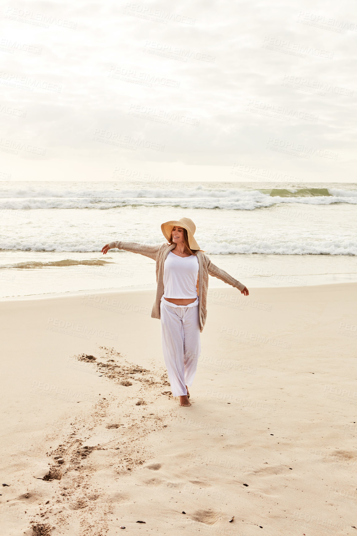 Buy stock photo Shot of a young woman standing with her arms outstretched at the beach