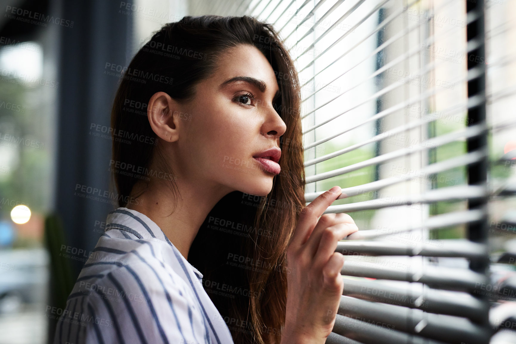 Buy stock photo Cropped shot of an attractive young woman looking through her window while standing indoors at home