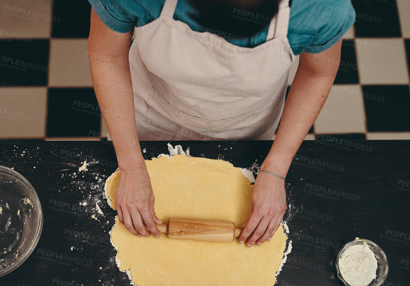 Buy stock photo Cropped shot of an unrecognizable woman flattening dough with a rolling pin while baking inside her kitchen at home