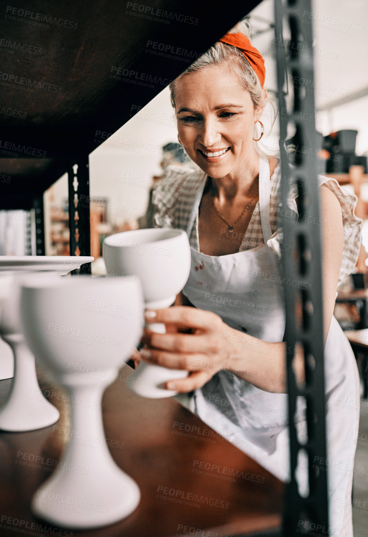 Buy stock photo Cropped shot of an attractive mature woman standing and organising her pottery on a shelf in her workshop