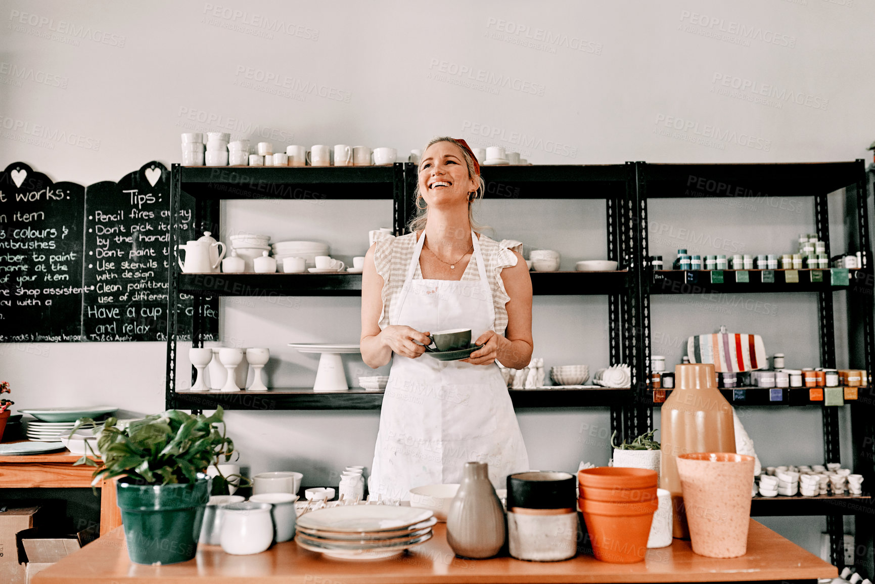 Buy stock photo Cropped shot of an attractive mature woman standing alone and holding a cup of coffee in her pottery workshop