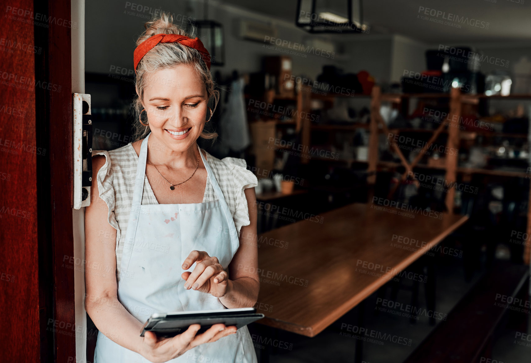 Buy stock photo Cropped shot of an attractive mature woman standing alone and using a tablet in her pottery workshop