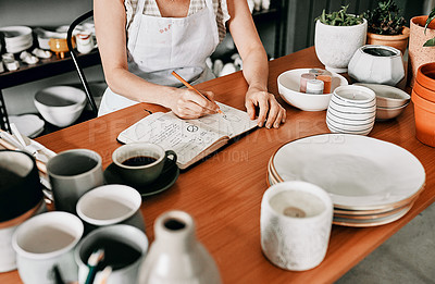 Buy stock photo Cropped shot of an unrecognizable woman sitting and sketching in a notebook in her pottery workshop
