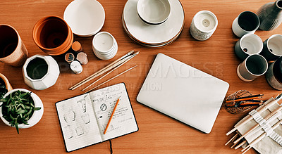 Buy stock photo High angle shot of a potter's sketches in a notebook and her laptop on a work desk in her workshop