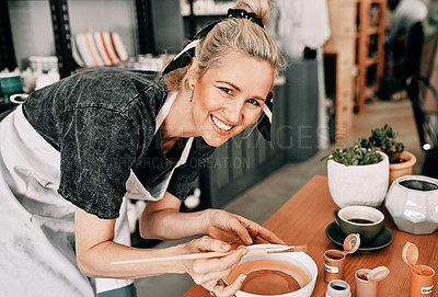 Buy stock photo Cropped portrait of an attractive mature woman standing alone and painting a pottery bowl in her workshop