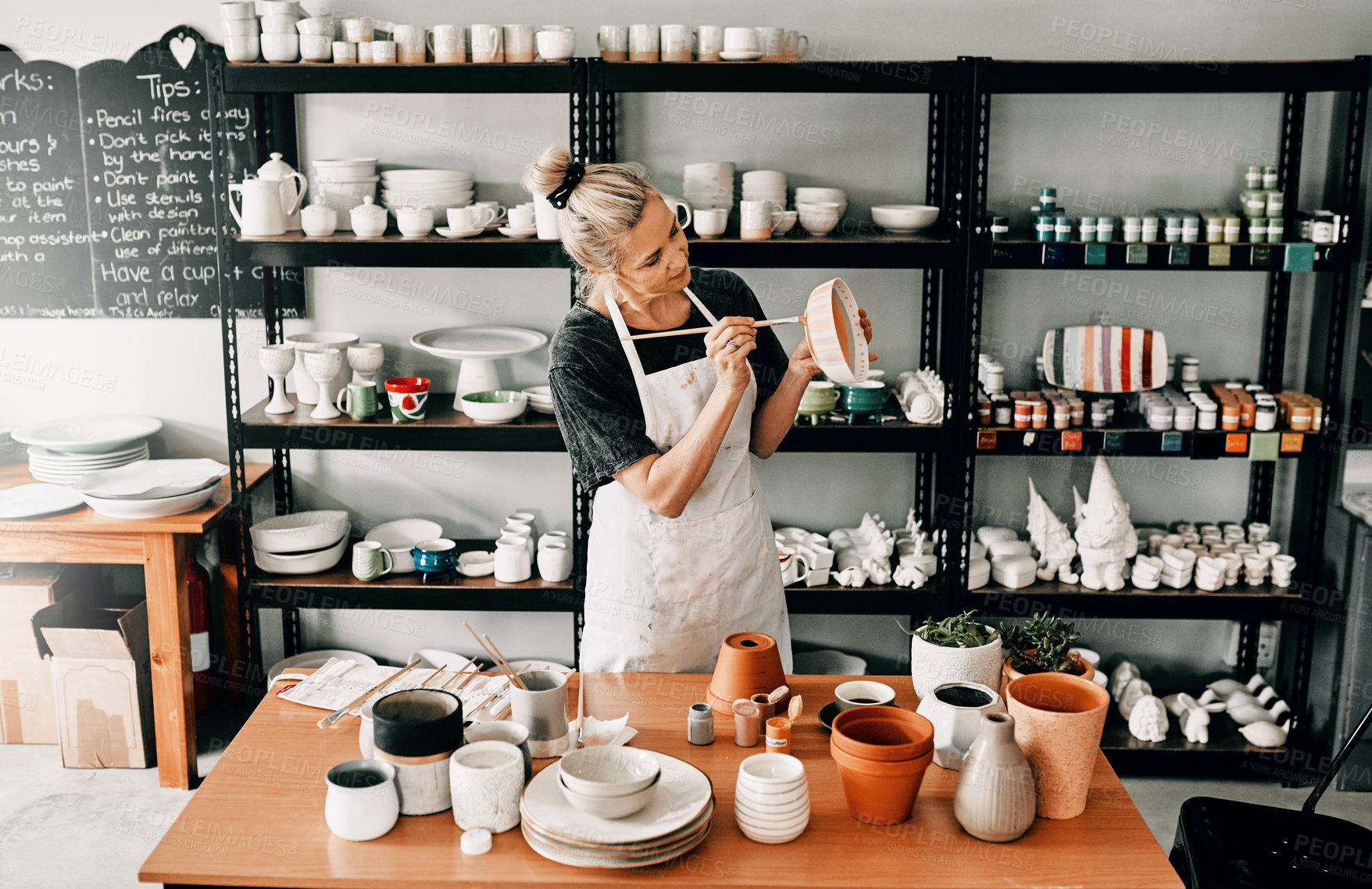 Buy stock photo Cropped shot of an attractive mature woman standing alone and painting a pottery bowl in her workshop