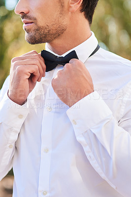 Buy stock photo Cropped shot of an unrecognizable young bridegroom putting on a bowtie while standing outdoors on his wedding day