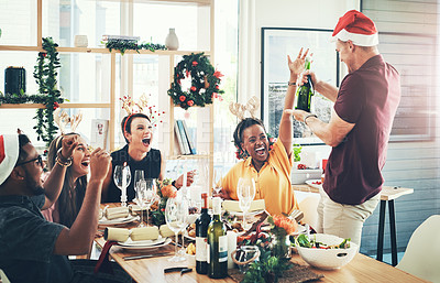 Buy stock photo Cropped shot of a handsome young man popping champagne while dining with his friends at Christmas